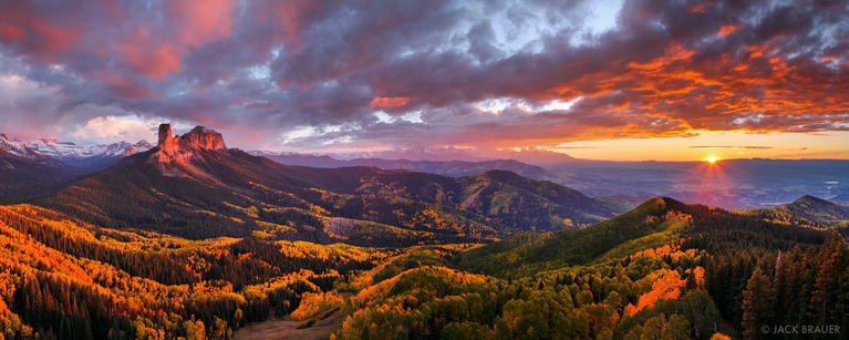 Sunset views of landscape with yellow-orange aspen trees in the foreground, snow-capped mountains in the background, and colorful clouds above